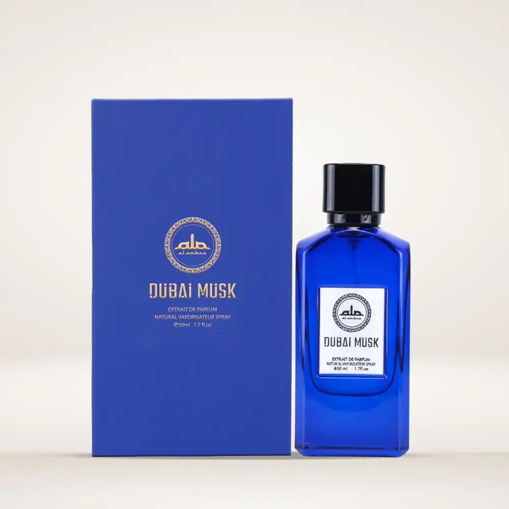 The Al Ambra Perfumes Dubai Musk Extrait de Parfum product set, showcasing a cobalt blue glass bottle with a white and gold label, positioned next to its matching rectangular blue retail box. Both items display the Al Ambra Perfumes logo and "DUBAI MUSK", with "Extrait de Parfum 50 ml / 1.7 Fl.oz." in gold text, against a light background.